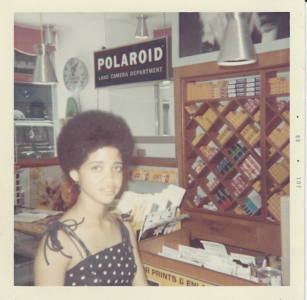 Girl with Afro in polka dot dress in camera store by Unknown