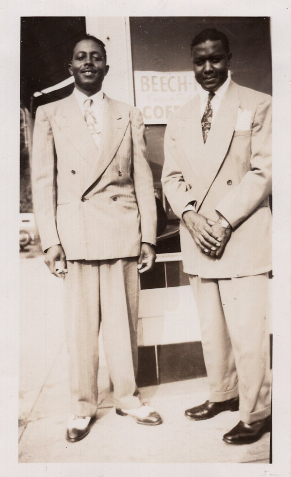 Two men in double-breasted suits in front of Beech-Nut coffee sign by Unknown