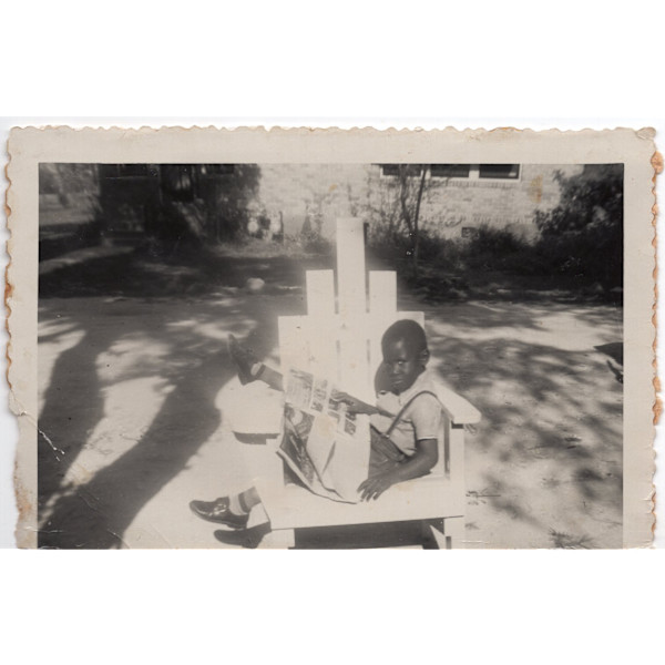Boy lounging outside with newspaper by Unknown