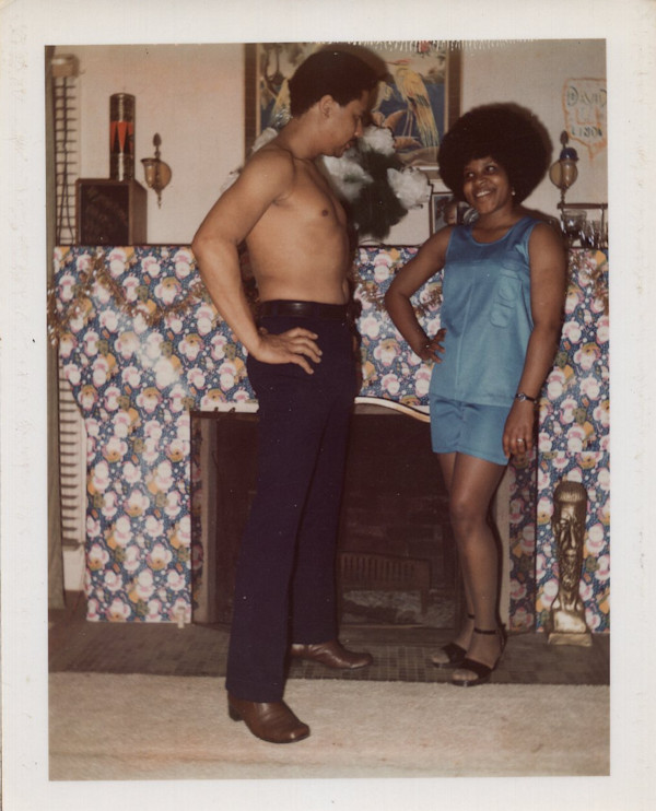 Shirtless man and woman with Afro in front of fireplace by Unknown