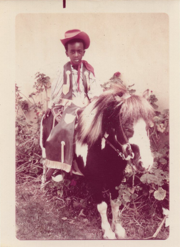 Young boy in cowboy hat on prop pony by Unknown