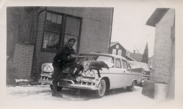 Man with rifle and dead deer on hood by Unknown