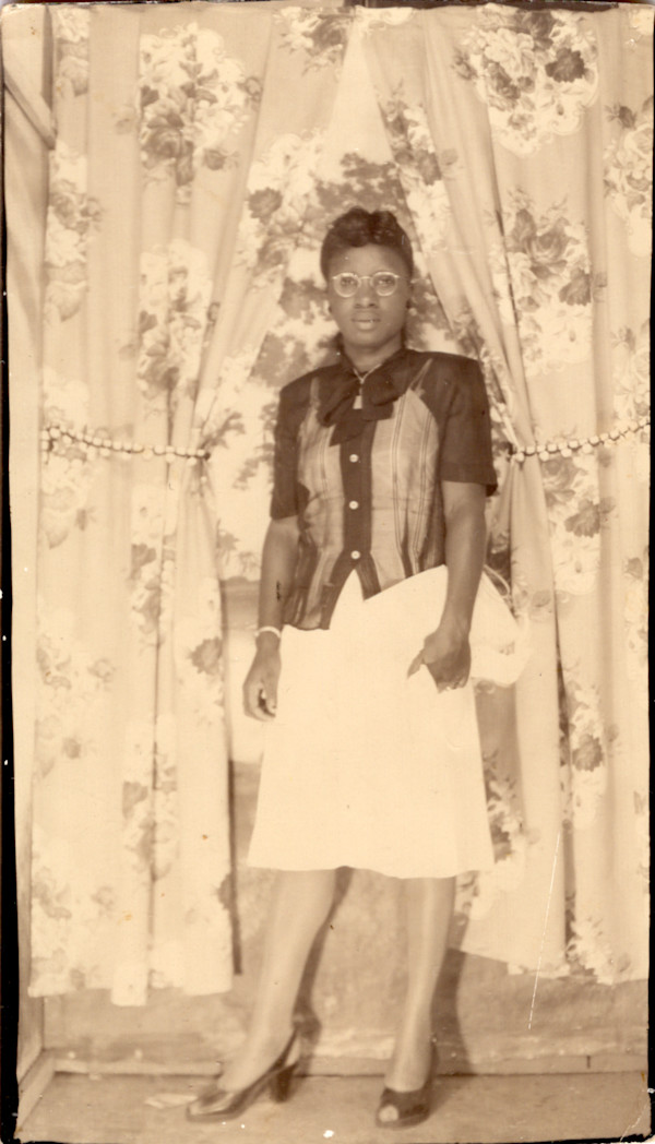Arcade portrait of woman against floral curtains holding handbag by Unknown