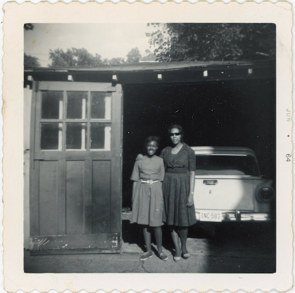 Women and girl standing at open garage by Unknown