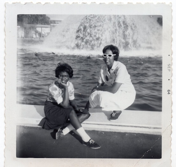 Woman in sunglasses and woman in eyeglasses by fountain by Unknown