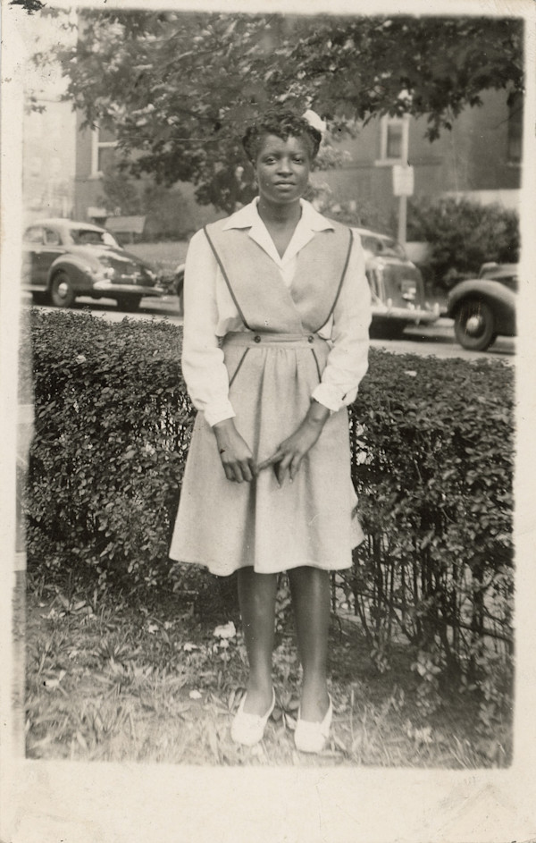 Young woman standing by hedge by Unknown