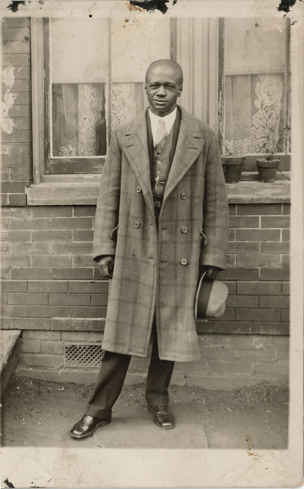 Man standing outside of windows with lace curtains by Unknown