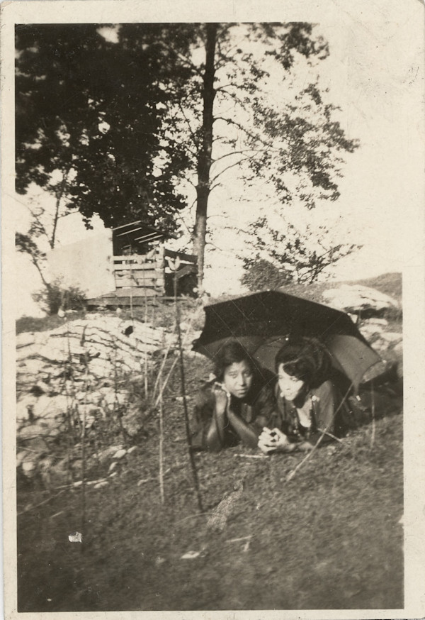 Two women lying on the grass under an umbrella by Unknown