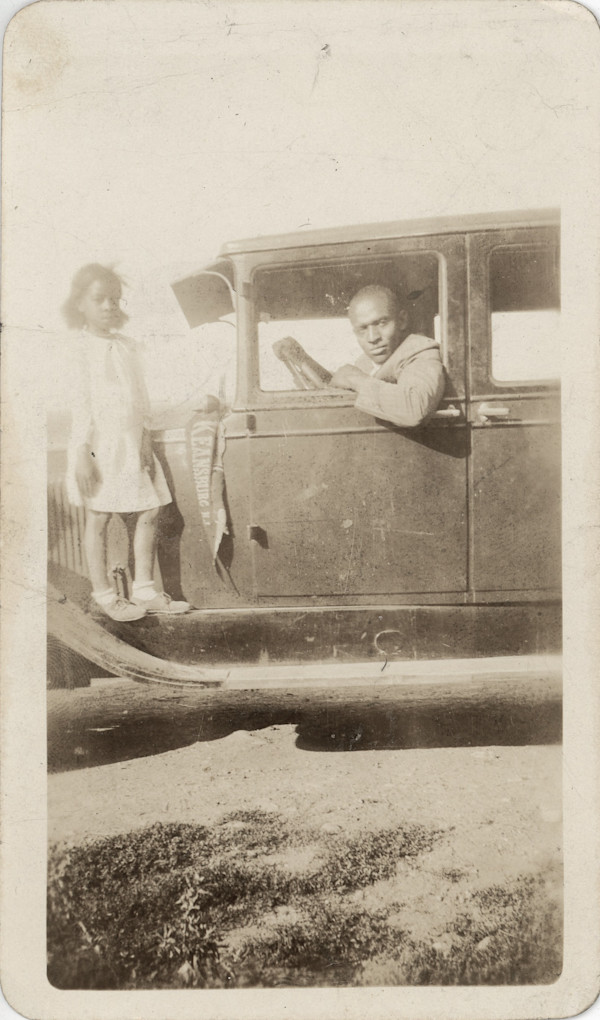 Man behind wheel of automobile with girl standing on running board with Keanesburg NJ pennant by Unknown