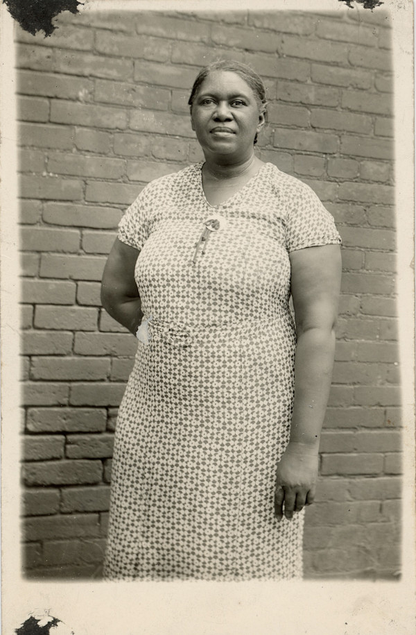 Woman standing next to brick wall by Unknown
