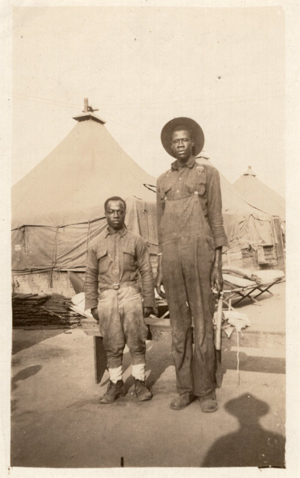 Tall man & small man outside of tents by Unknown