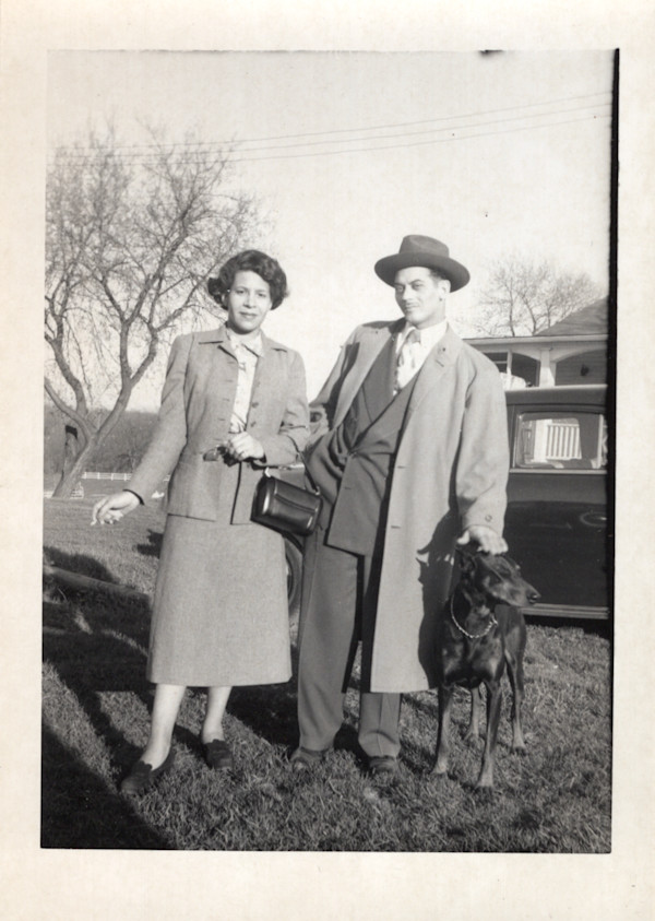 Couple in front of house and car with dog by Unknown