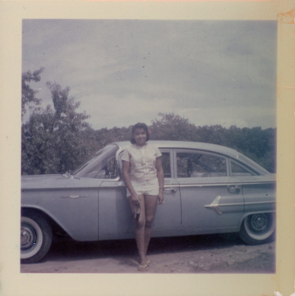 Girl with camera leaning against car by Unknown