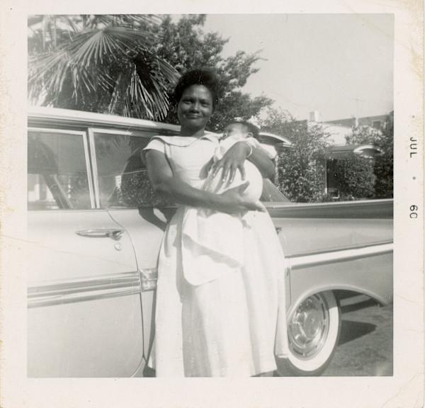 Woaman holding infant next to automobile by Unknown
