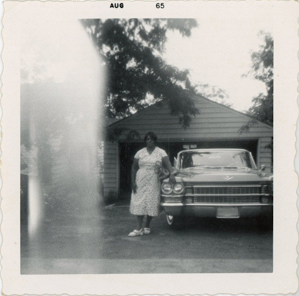 Woman standing next to automobile in front of garage by Unknown