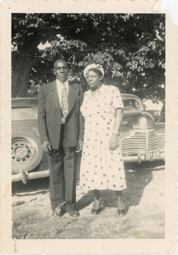 Couple posed near automobiles by Unknown