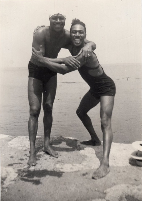Two men in swimsuits playfully embracing at the beach by Unknown