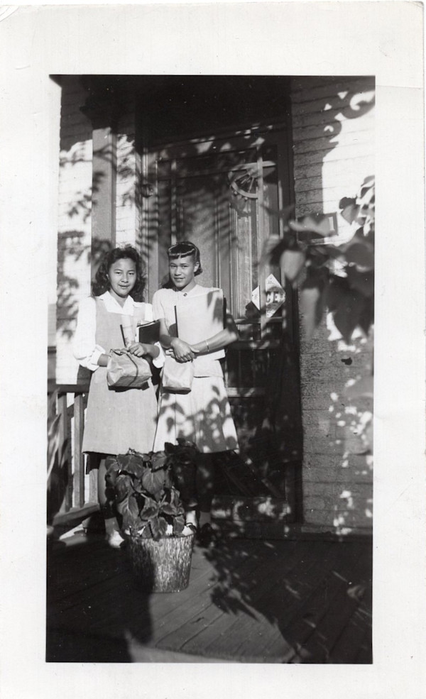 Two schoolgirls holding books and lunchbags by Unknown