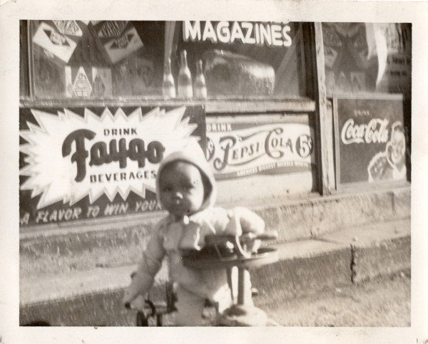 Infant in front of store window signs by Unknown