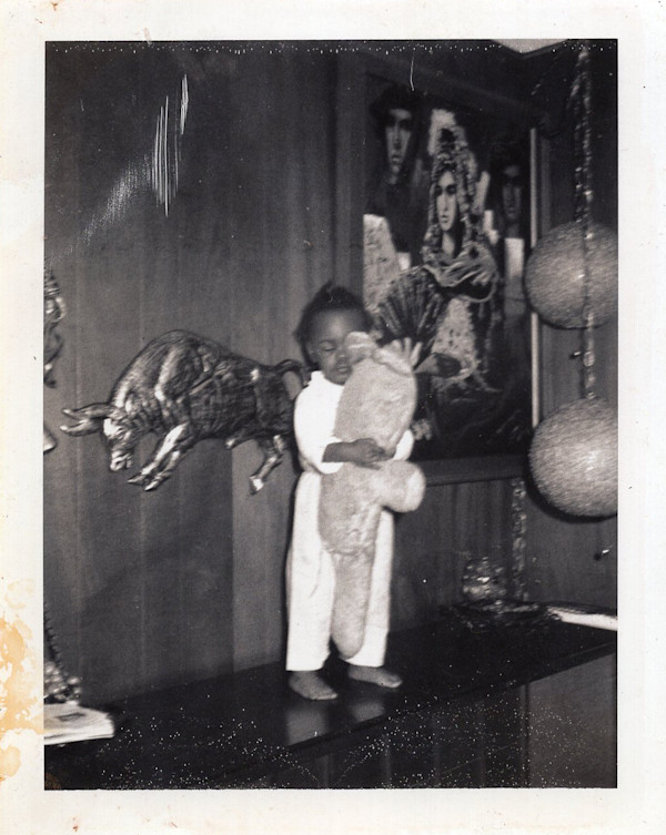 Child with eyes closed holding stuffed animal in room with Spanish art by Unknown