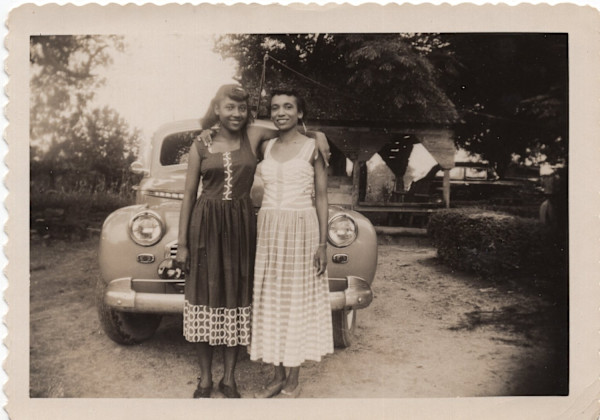 Two women in sundresses hugging by Unknown