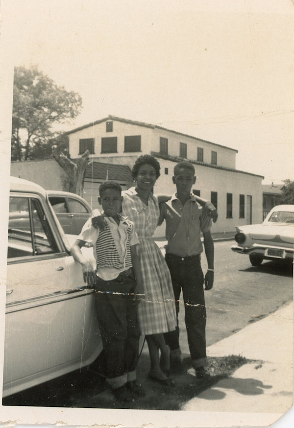 Woman with two boys leaning against car by Unknown