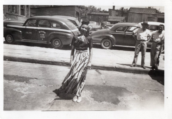Woman in plaid maxi skirt near Bison Cab Association taxicab by Unknown