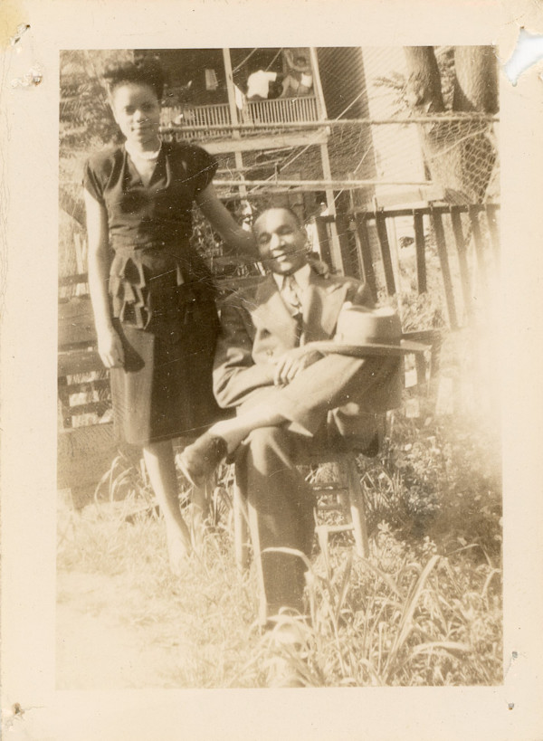 Woman standing, man seated outdoors by Unknown
