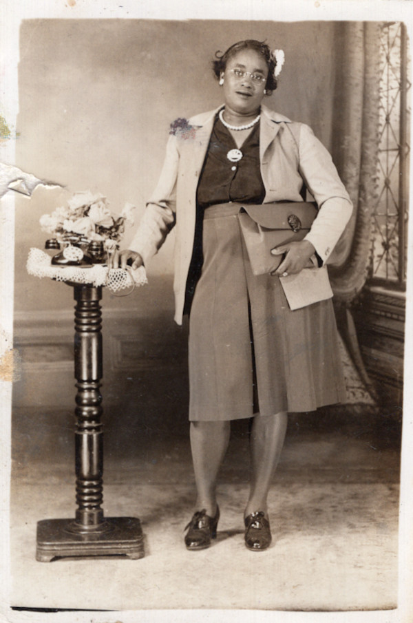 Woman clutching satchel with hand on pedestal by Unknown