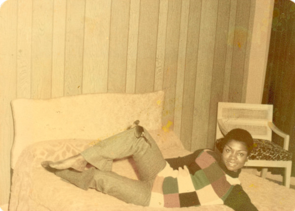 Reclining woman in checkerboard sweater balancing sunglasses on her knee by Unknown