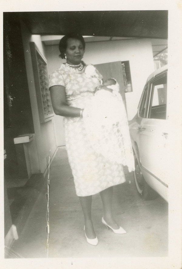 Woman holding infant in driveway by Unknown