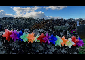 Lei over gravestone, rock wall and sky, St Michael's urupā, Ōhaeawai, 30 April 2021