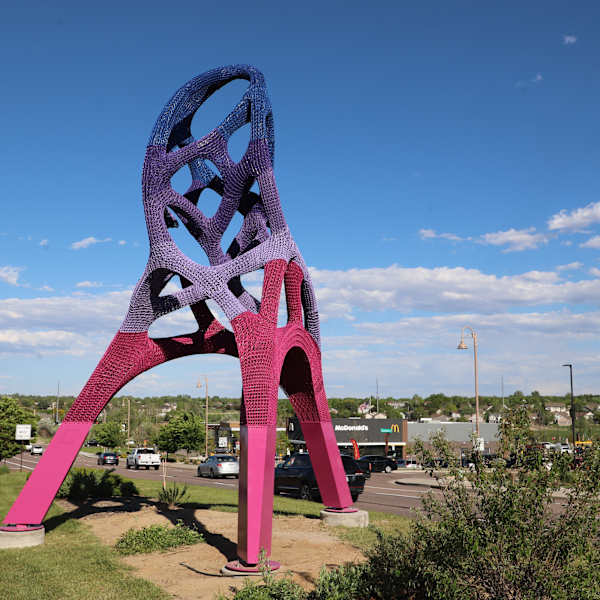 Tall, colorful abstract sculpture on a green median.