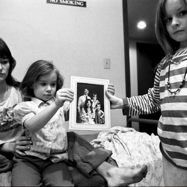 Mary + her daughters holding a family portrait with their father, Minneapolis, from Living with the Enemy by Donna Ferrato, Image 1.