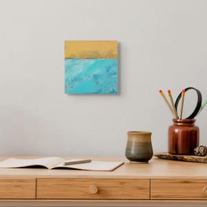 "Landscape #4" by Steven McHugh  Image: Room view of "Landscape #4," a small abstract landscape measuring 8" x 8" x 2.5". This oil and cold wax artwork presents a striking view from the water of Long Island off Madeline Island and the Apostle Islands. Crafted by  Island artist Steve McHugh, it features bold, contrasting colors and textures of teal and yellow with a distinct strip of color across the panel. This versatile piece on wood panel can be proudly displayed on your wall or placed on a shelf. Price includes shipping in the U.S

The abstract landscape  painting is divided into two distinct horizontal sections. The upper portion of the canvas features a warm, earthy yellow color, with subtle variations and textural strokes that add depth and complexity. The lower section is dominated by a cool, vibrant turquoise, with streaks and patches of varying shades of blue and white, suggesting a sense of movement or fluidity. The contrasting colors and textures between the two sections create a dynamic and visually engaging composition.