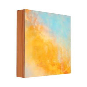 "Clouds" by Steven McHugh  Image: Side view "Clouds," an 8" x 8" oil and cold wax painting on wood panel by Steve McHugh,  abstract painter based on Madeline Island. This versatile piece can effortlessly enhance your space, standing  on a shelf or hanging elegantly with the wire installed on the back.  "Clouds" comes ready to hang and includes shipping within the U.S. Add a touch of Steve's island-inspired artistry to your home or office with this unique, mixed-media gem. 

The artwork is an abstract painting featuring a dynamic blend of colors. Dominant hues of orange and blue create a vibrant contrast, with the orange occupying more of the painting's bottom and central areas, and the blue filling much of the upper section. The colors merge and overlap in soft, layered patterns, giving a sense of depth and fluidity. The texture of the paint is varied, including both smooth gradients and rougher, more textured areas, adding to the visual interest and complexity of the piece.