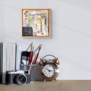 "Deconstructed #5" by Steven McHugh  Image: Room view of "Deconstructed #5",  a small original mixed media collage painting by Madeline Island artist Steve McHugh. This unique piece is constructed of layers of canvas, cardboard on wood panel with oil, cold wax, spray paint, graphite, and crayon. Measuring at 8" x 8" and framed in a natural wood finished gallery floating frame, this artwork is a stunning addition to any art collection. The signature red thumbprint in the lower right corner adds a personal touch to this captivating piece. Bring a touch of modern art to your home with "Deconstructed #5".

The artwork is an abstract painting that contains a mix of colors and textures applied on a canvas and enclosed within a wooden frame. The painting features various elements and materials, including multiple splatters of paint, reminiscent of the Jackson Pollock style. 

Prominent colors include yellow, black, grey, and blue, with some red and white highlights. There are splatter effects and brushstrokes creating a sense of movement and randomness. To the left, there are black and white, patterned circular shapes arranged vertically. Below them, there's a section with horizontal black and white stripes. The background seems layered, with off-white, grey, and muted blue tones blending together.

This abstract composition evokes a sense of spontaneity and dynamic energy, with a rich interplay of colors and textures.

Shipping costs and sales tax will be added after destination is determined.