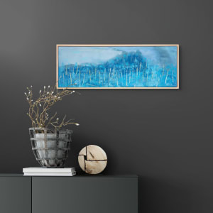 "Winter Blues" by Steven McHugh  Image: Room view of the captivating "Winter Blues" painting by Steve McHugh. Measuring 10" x 30", this abstract landscape piece brings to life the icy chill and tranquility of the season with its cool blue tones. Created using oil and cold wax on wood panel, the piece is textured and layered, adding depth and dimension to the artwork. The simple wood gallery floating frame completes the piece, making it ready to hang and display in any space. Add a touch of winter beauty to your art collection with this stunning painting.

This  landscape painting that predominantly features various shades of blue, creating an ethereal, wintry scene. The use of light and dark tones of blue gives a sense of depth and texture to the background, which suggests a foggy, mist-filled atmosphere. The landscape is dotted with vertical, tree-like structures rendered in lighter hues of yellow and white, adding contrast and drawing the viewer's eye throughout the piece. The overall composition evokes a tranquil, serene environment, with the cool colors and abstract forms contributing to a sense of calm and isolation.

Shipping and sales tax is added after destination is determined.