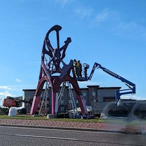 People in a lift assemble a tall sculpture.