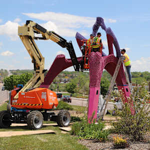 People in a lift assemble a tall sculpture.