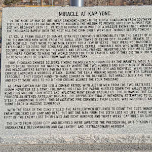 Korean War Memorial by Jerime Hooley  Image: Photograph by Jacob B. Arnell. Licensed by Creative Commons (CC BY-SA).

Here is the transcription of the text from the plaque:

MIRACLE AT KAP YONG

On the night of May 26, 1951, near Sanchon–Jonc-Ni, So. Korea, Guardsmen from Southern Utah's 213th Field Artillery Battalion were assigned the mission to provide artillery support for the 21st Inf. Regiment, 24th ID. Patrols returned with word of a massive enemy force numbering in the thousands barely over the next hill. The grim order went out: "Nobody sleeps tonight!"

Lt. Col. J. Frank Dalley of Summit, Utah, felt enormous responsibility for the safety of his men. The six hundred men were from the small Utah towns of Cedar City, Fillmore, Beaver, St. George, and Richfield. They were young men, except for a few officers. They were not hardened, experienced soldiers, but scholars and farmers. Gentle, honorable men who were also brothers, cousins, uncles, or neighbors—relatives or lifelong friends. Nevertheless, they were convinced they were fighting to make the world safe for their families, and if they did their job well, their sons might be spared from war in their turn.

Four thousand Chinese soldiers, finding themselves surrounded by the infantry, made a desperate bid to break through the narrow valley where the two hundred and forty men of Headquarters and Headquarters Battery and Battery A (units from Cedar City and Richfield) were located. The Chinese launched a vigorous attack. During the early morning hours, the fight for survival was ferocious. They fought hand-to-hand combat in the darkness. But miraculously, the two hundred and forty were able to hold their ground against the four thousand.

At dawn, Captain Ray Cox led a combat patrol with just 18 men from the two batteries using a 105mm howitzer as a tank. Following his lead, the patrol hurtled down the valley, destroying numerous machine-gun nests and inflicting many enemy casualties. The remaining five guns provided an intense artillery barrage. The opposition finally withdrew after attempting to climb the steep surrounding slopes. This devastating fire convinced them escape was impossible, and they turned back in massive surrender.

With the roar of the guns stilled, the artillerymen returned to count the cost. Hundreds of enemy soldiers lay limp and dead, but not one man from the 213th lost his life. Three hundred and fifty of the enemy lost their lives, and 830 were captured or surrendered.

The units from Cedar City and Richfield were awarded the Presidential Unit Citation for their "unshakeable determination and gallantry" and "extraordinary heroism."