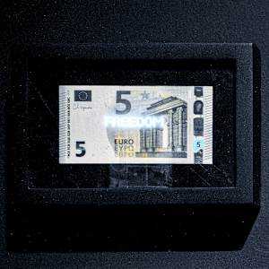 Planetary Values- 5 Euro Bill - Freedom by Jorge Luis Vaca Forero  Image: Planetary Values- 5  Euro Bill / (Freedom) is a unique approach to global politics. It focuses on the Euro bill, one of the main currencies in the world economy. This project highlights the most frequently mentioned values from the European Union’s Constitution by using laser cuttings to create perforations in the bills, which are then illuminated by LED lights.

The aim is to challenge the legitimacy and symbolic significance of the State. It does this by connecting the symbolism of money with the economy it represents and the values and commitments made by governments that are often not met around the world. The words on the bills can only be seen when illuminated, emphasizing their hidden nature.

This initiative turns these bills into seemingly useless objects and invites us to reconsider the global significance of currency. It questions the ideals of peace, well-being, and democracy that nations claim to uphold for their citizens, suggesting that these ideals may not be fully realized and are limited by the currency that represents economic and social exchanges.
