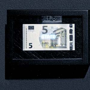 Planetary Values- 5 Euro Bill - State by Jorge Luis Vaca Forero  Image: Planetary Values- 5  Euro Bill / (State) is a unique approach to global politics. It focuses on the Euro bill, one of the main currencies in the world economy. This project highlights the most frequently mentioned values from the European Union’s Constitution by using laser cuttings to create perforations in the bills, which are then illuminated by LED lights.

The aim is to challenge the legitimacy and symbolic significance of the State. It does this by connecting the symbolism of money with the economy it represents and the values and commitments made by governments that are often not met around the world. The words on the bills can only be seen when illuminated, emphasizing their hidden nature.

This initiative turns these bills into seemingly useless objects and invites us to reconsider the global significance of currency. It questions the ideals of peace, well-being, and democracy that nations claim to uphold for their citizens, suggesting that these ideals may not be fully realized and are limited by the currency that represents economic and social exchanges.
