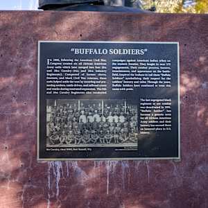 Buffalo Solider by Chris Navarro  Image: Bronze Plaque mounted on a sculpture base, it says:
"BUFFALO SOLIDERS"
"In 1866, following the American Civil War, Congress created six all-African American Army units, which later merged into four (9th and 10th Cavalry -24th and 25th Infantry Regiments). Composed of former slaves, freemen, and black Civil War veterans, these units helped settle the West by escorting and protecting settlers, cattle drives, and railroad crews and tracks during westward expansion. The 9th and 10th Cavalry Regiments also conducted campaigns against American Indian tribes on the western frontier. They fought in over 175 engagements. Their combat prowess, bravery, tenaciousness, and appearance on the battlefield inspired the Indians to call them "Buffalo Soldiers" symbolizing their respect for the soldiers' bravery and valor. Through the years, Buffalo Soldiers have continued to wear this name with pride.
The last segregated black regiment to see combat was deactivated in 1951.
"Buffalo Soldier" has become a generic term for all African American Army soldiers, and their bravery has earned them an honored place in the U.S."