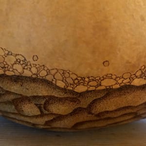 Riverbowl III by Serena Kovalosky  Image: Photo #8
Woodburning. The "earth" foundation always takes the longest - hundreds of tiny dots! - and is now complete. Next are the river stones. They are among my favorite part of any river - tumbled smooth by years of water flowing over and around them. Each one has a story. I will often stand at the edge of the river and look straight down, exploring its many colorful "jewels" at the bottom, and along the shoreline. 

Their smoothness is a testament to the effects of time, even on the most durable. Some have traveled many miles. A flooded river means more may continue their travels. They always look magical under the moving water. If I am attracted to one and bring it out of the water, it loses its shine as it dries in the sun. Some I keep because they speak to me, but I generally leave them where they belong. Maybe they will share their stories with others as well.