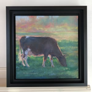 Contentment by Crystal Beshara  Image: "Contentment" captures a quiet, fleeting moment as a solitary cow grazes peacefully in the cool hush of a late summer evening. Bathed in the hazy, golden last rays of sunlight, the surrounding pasture breathes serenity while soft, atmospheric edges evoke a sense of timeless calm.

This intimate, small-scale piece celebrates the renewed beauty found in everyday farm life. The muted tones, diffused light, and tender observation of detail invite viewers to pause, reflect, and experience the gentle tranquility of the rural landscape.