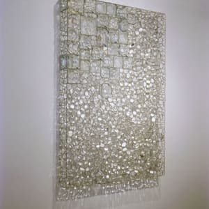 Transparency by Richard Klein  Image: Alt Text Long Description: A rectangular wall sculpture composed of numerous translucent glass squares and pebble shapes arranged in a grid-like pattern. The glass squares vary in size and are overlaid with smaller, irregularly shaped glass pieces resembling pebbles. The composition appears somewhat three-dimensional, with the texture and positioning of the glass elements casting subtle shadows on the wall behind. The sculpture exhibits a range of reflective and refractive qualities due to the interplay of light with the glass, creating a shimmering effect. The background is a simple, light-colored wall that contrasts with the intricate surface of the artwork. Note: the alt text was written with support from the ASU Image Accessibility Creator AI tool.