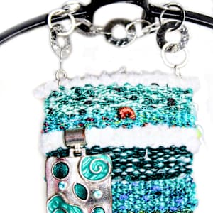 Teal Rejuventation Mini Art Tapestry by Annette  Image: Hand woven yarns make a perfect backdrop to this piece of jewelry. Check out the circles that made up this bracelet   hanger. 