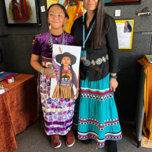 Legend of the Mocking Jay by Karen Clarkson  Image: August 2023 photo of artist and model at the Santa Fe Indian Market. AtsaBiyaazh accepting a reproduction of the portrait “The Mocking Jay” with her family. See additional image to see the creation of this piece.