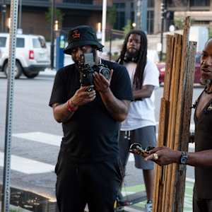Installation, Marlon Hall by Shelby Head  Image: Warren Queton invited viewers at the opening reception of Beyond the Whitewash at Living Arts of Tulsa to join Marlon Hall at the corner of Martin Luther King Blvd and Reconciliation Way, where, on March 22, 2023, Marlon was racially profiled and detained by force for a crime he didn’t commit. On the street corner, Marlon talked about his experience, Phetote Mshari performed a poem, and Warren Queton offered a prayer through song. Carrying a mask for his installation in the exhibition, Marlon led the processional back to the opening reception at Living Arts, where prayer, poetry, and song continued.